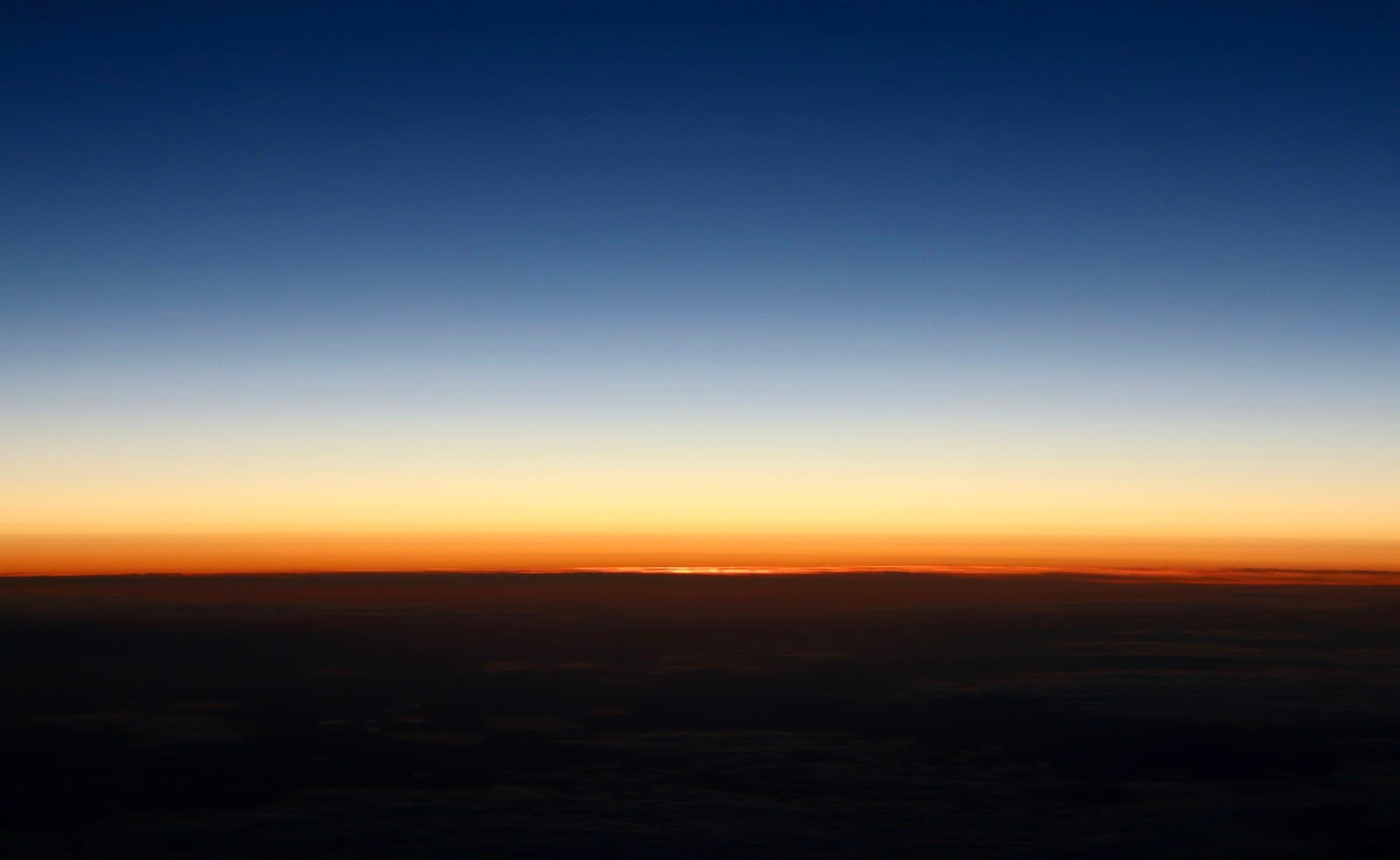 Expansive horizon where land meets sky at dusk, deep charcoal foreground fading to muted gold light.