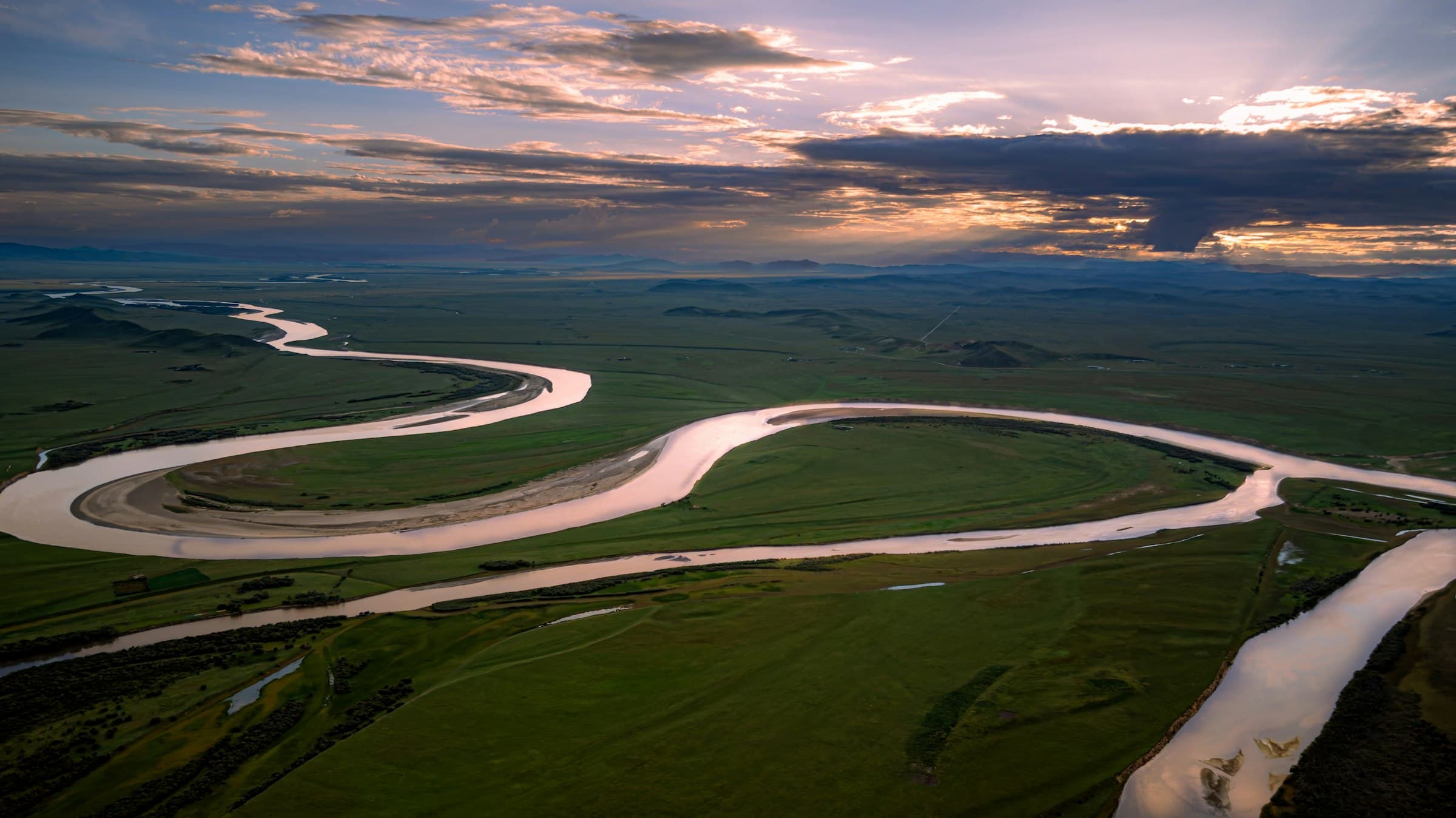 Cinematic wide aerial of a vast river winding through open plains at golden hour.